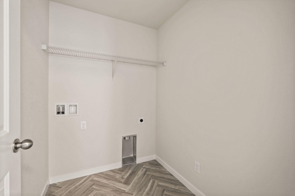 Narrow laundry room with wire shelf, hookups and herringbone-pattern vinyl floor.