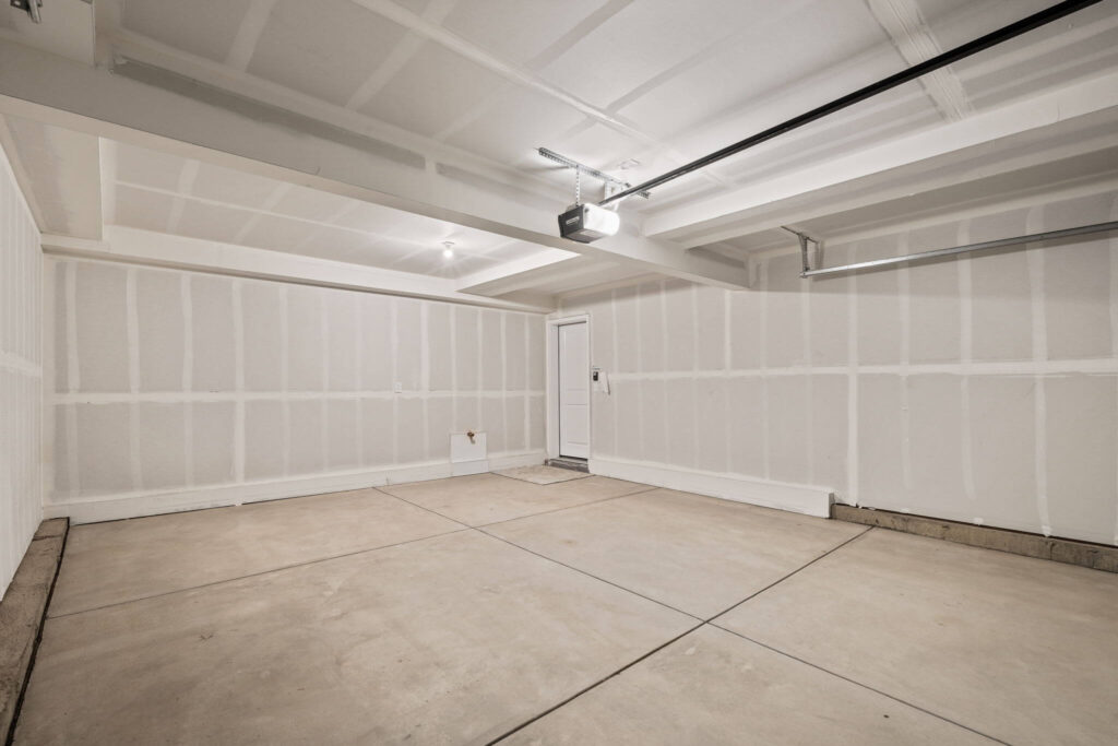 Alternate angle of an empty two-car garage showing entry door and garage opener.