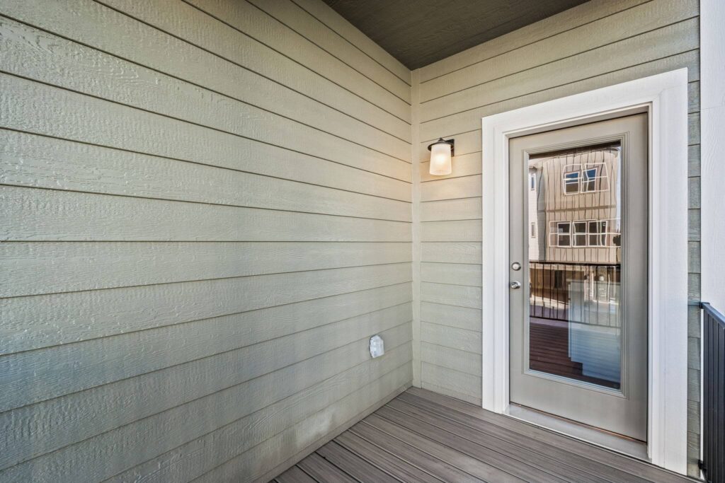 Covered balcony corner with glass-paneled door, wall sconce and horizontal siding.
