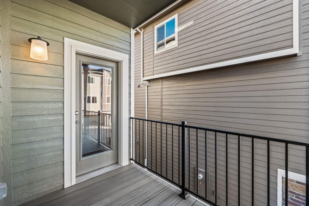 Small covered balcony with glass-paneled door, metal railing, and exterior siding.