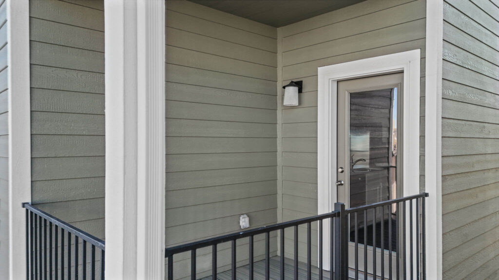 Covered exterior balcony with metal railing, glass door and mounted wall light.