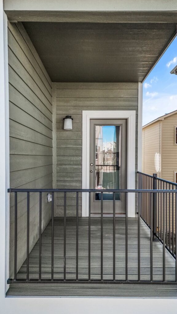 Small covered balcony with glass-paneled exterior door, horizontal siding and metal railing.