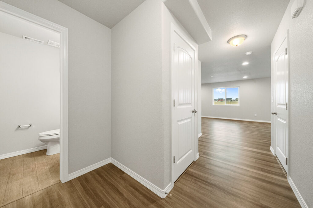 Interior hallway opening onto a large room with wood-look flooring and a small half bath visible.