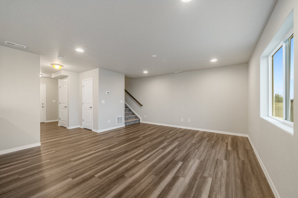 Spacious open living area with wood-look flooring, recessed lights, and a windowed wall.