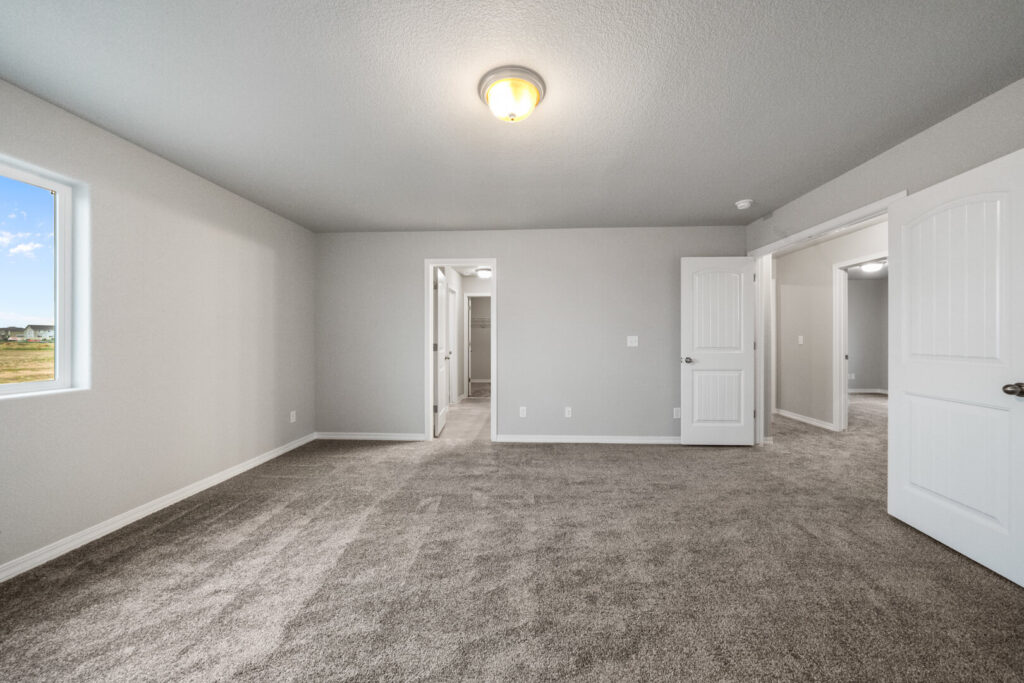 Empty carpeted bedroom with gray walls, single window, ceiling light, and open doorways.