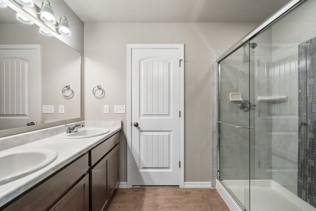 Bathroom with double vanity, tub/shower enclosure with glass doors, and a closed interior door.