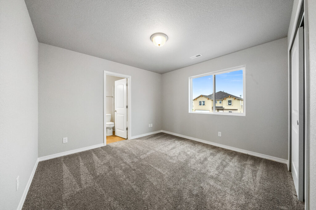 Empty carpeted bedroom with gray walls, window and doorway to a bathroom visible.