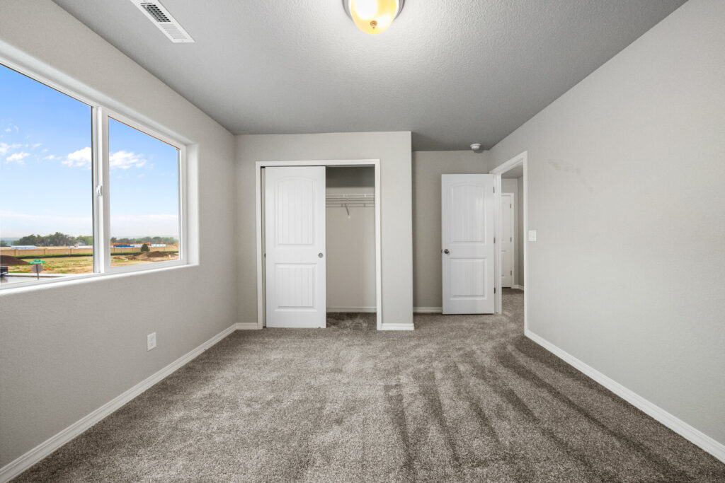 Another angle of the carpeted bedroom showing closet with sliding doors and large window.