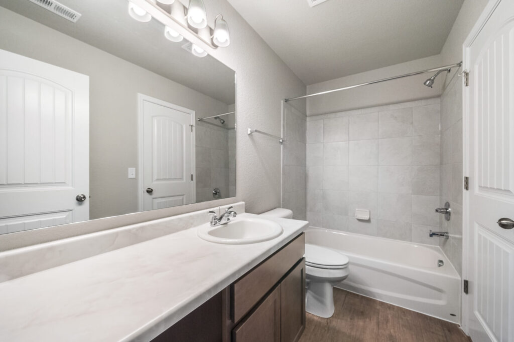 Bathroom with single vanity, large mirror and tub-shower with tiled surround.