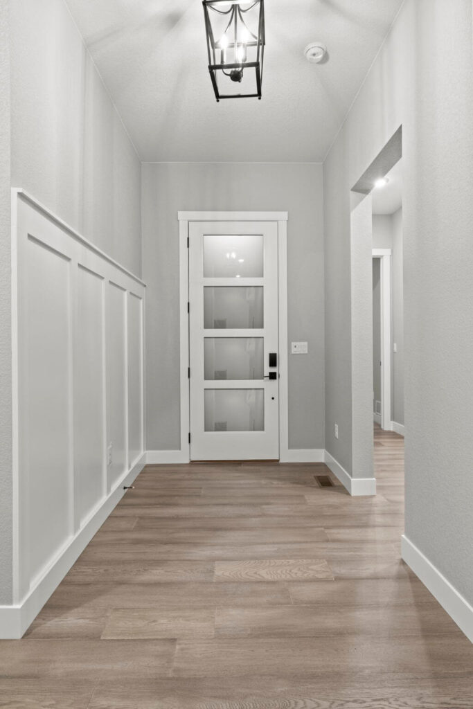 Interior entry hall with modern glass-panel front door, wainscot wall paneling, and wood-look flooring.