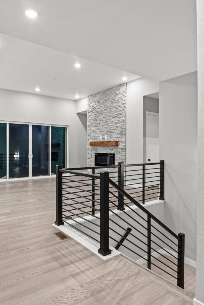 Interior living area with metal stair railing and stone fireplace wall, light wood floors.