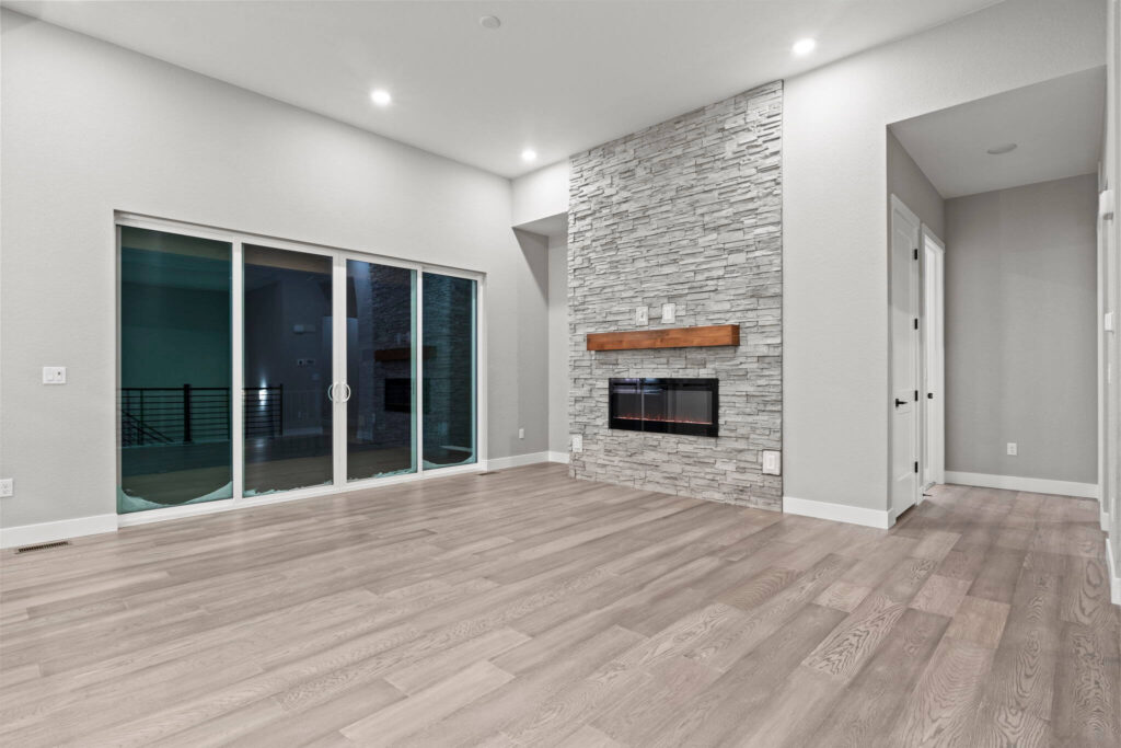 Empty living room with large sliding glass doors and stone fireplace on light wood floors.