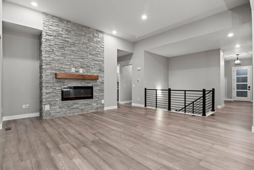Wide shot of open living room showing stone fireplace, stair railing, and entry hallway.