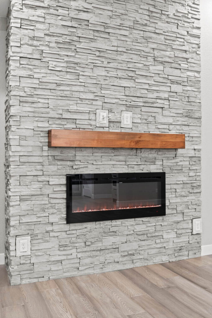 Stone-clad wall with recessed electric fireplace and narrow wooden mantel above.