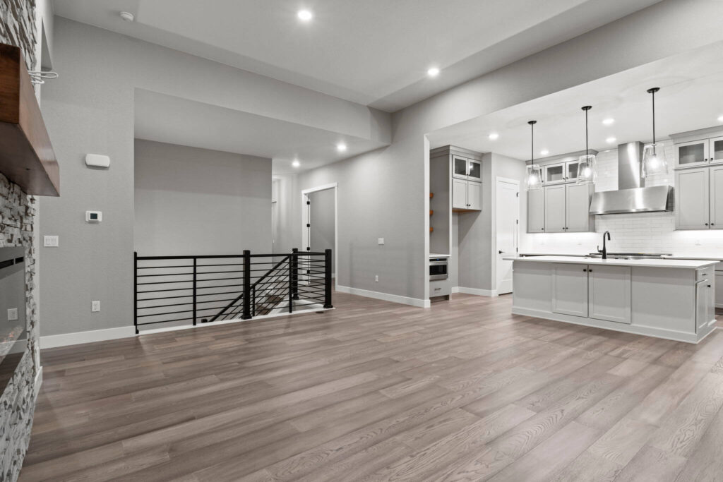 Open-plan living area with wood-look floors, stair railing, and kitchen visible in background.
