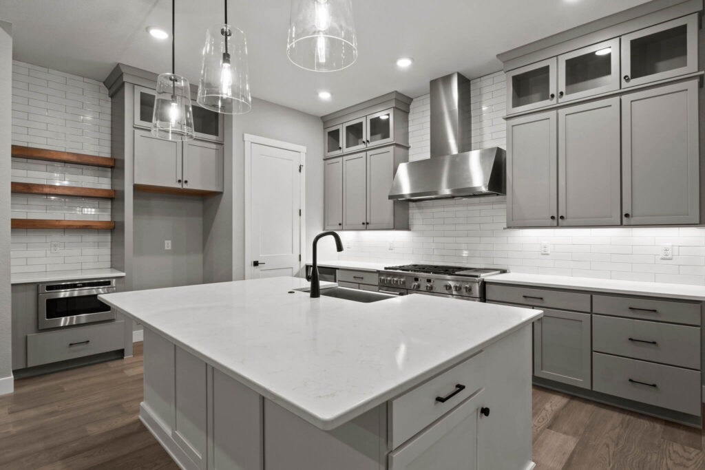 Modern kitchen with large center island, farmhouse sink, pendant lights, and gray shaker cabinets.