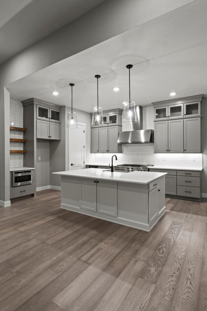 Open kitchen view from afar showing island, hanging glass pendants, and gray cabinetry.