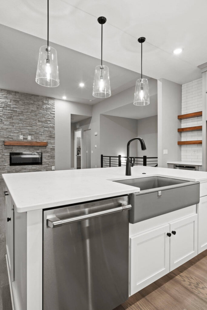 Close-up of island sink area with dishwasher, apron-front sink, and three glass pendant lights.