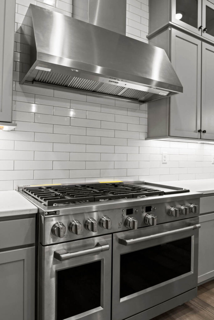 Close-up of stainless steel dual oven range and large vent hood against subway tile.