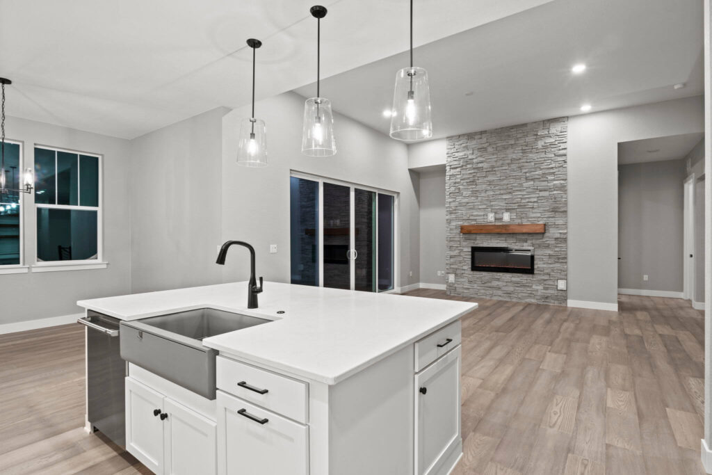 Open-concept living area with kitchen island, farmhouse sink, pendant lights, and stone fireplace.