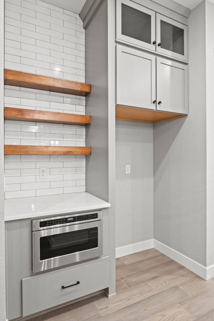Butler’s pantry area with built-in microwave, floating wood shelves, and upper cabinets.