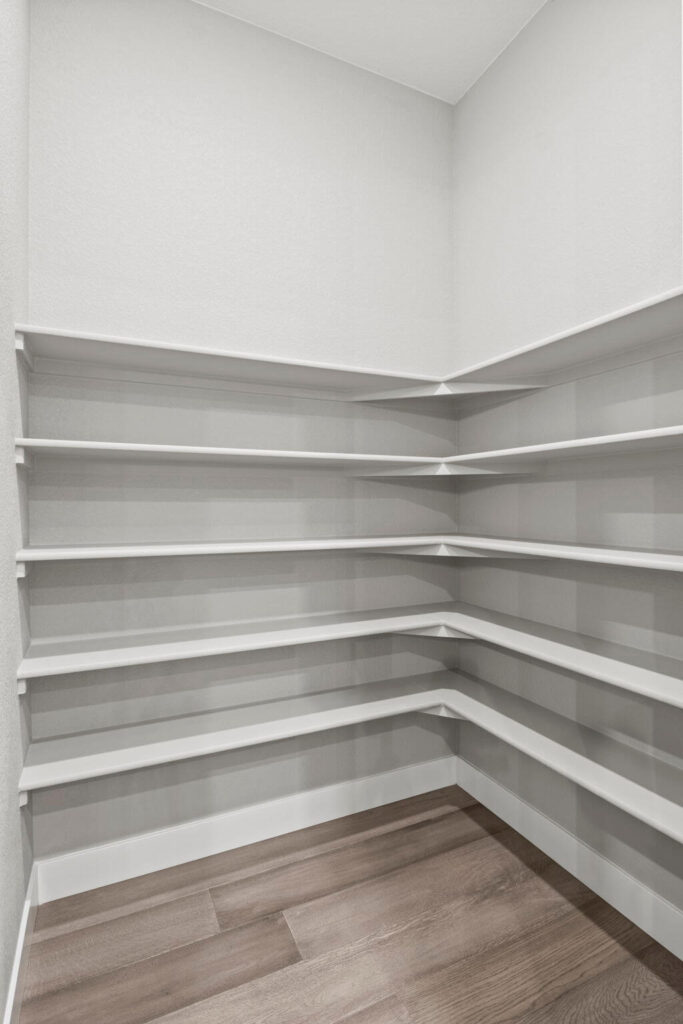 Corner pantry with multiple white built-in corner shelves and wood-look flooring.