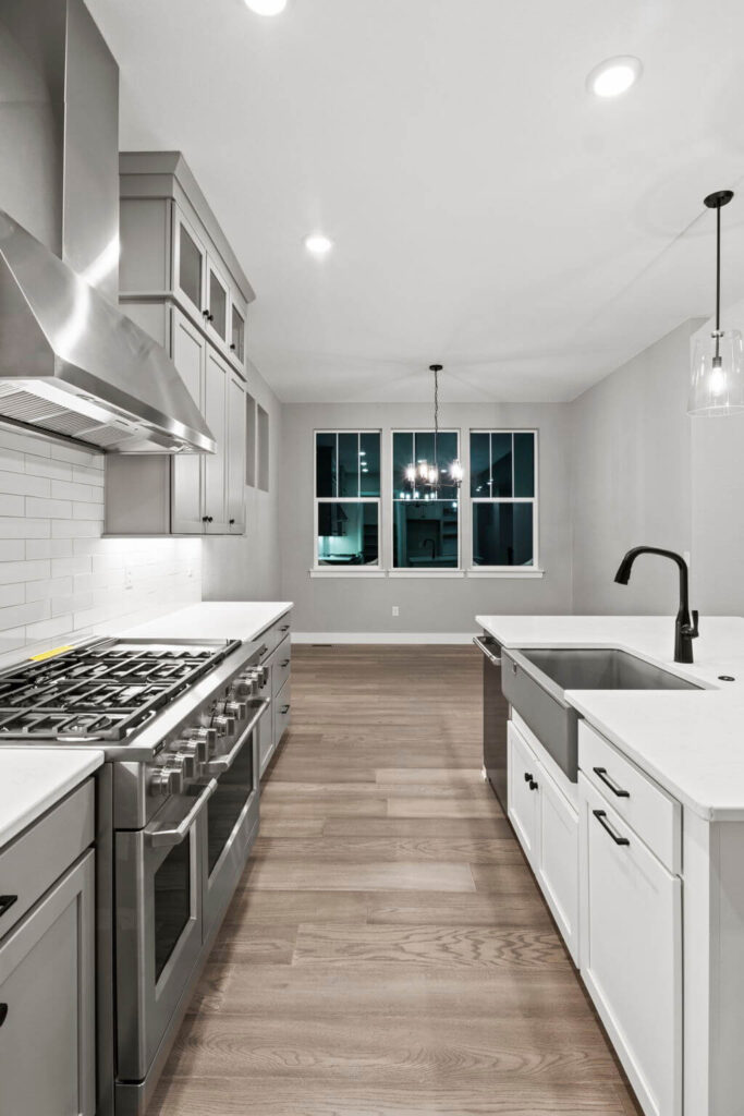 Modern kitchen galley view with stainless range, island sink, and pendant lights.