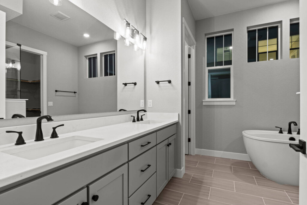 Bathroom vanity with double sinks, large mirror, and freestanding tub by a window.