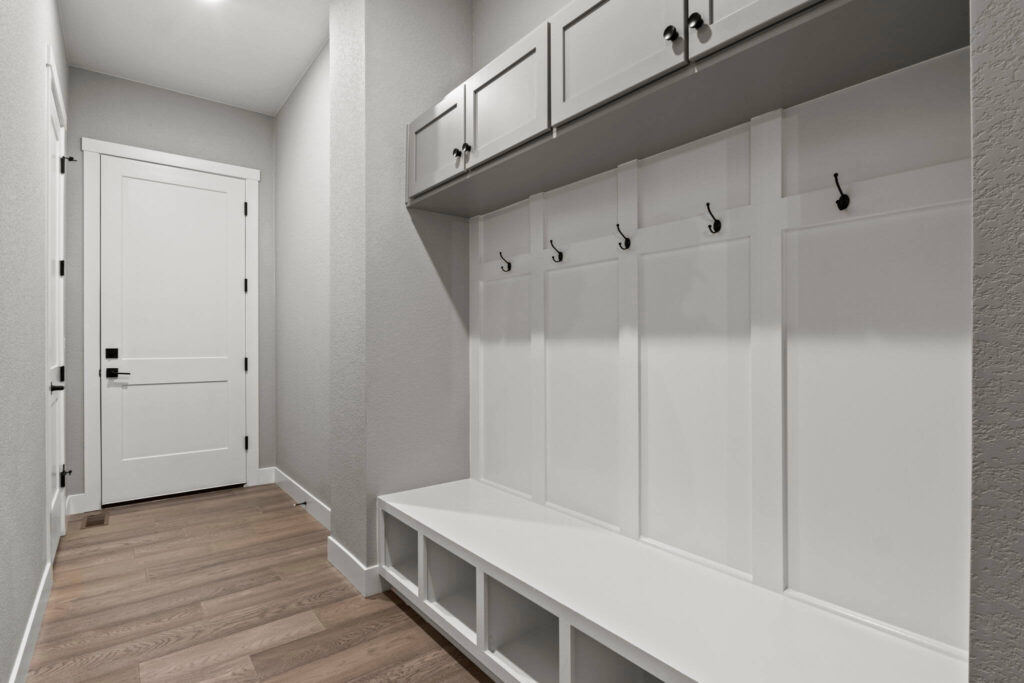 Mudroom-style bench with storage cubbies, coat hooks, and overhead cabinets in a hallway.