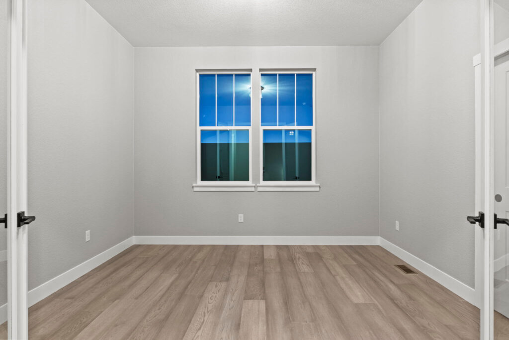 Empty rectangular room with two windows centered on the far wall and light wood-look flooring.
