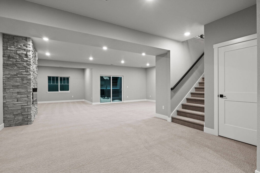 Large finished basement room with carpet, recessed lights, stone fireplace and stairs to upper floor.