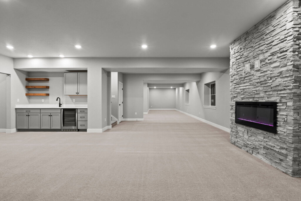 Finished basement with built-in wet bar, long open area, and stone fireplace with electric insert.