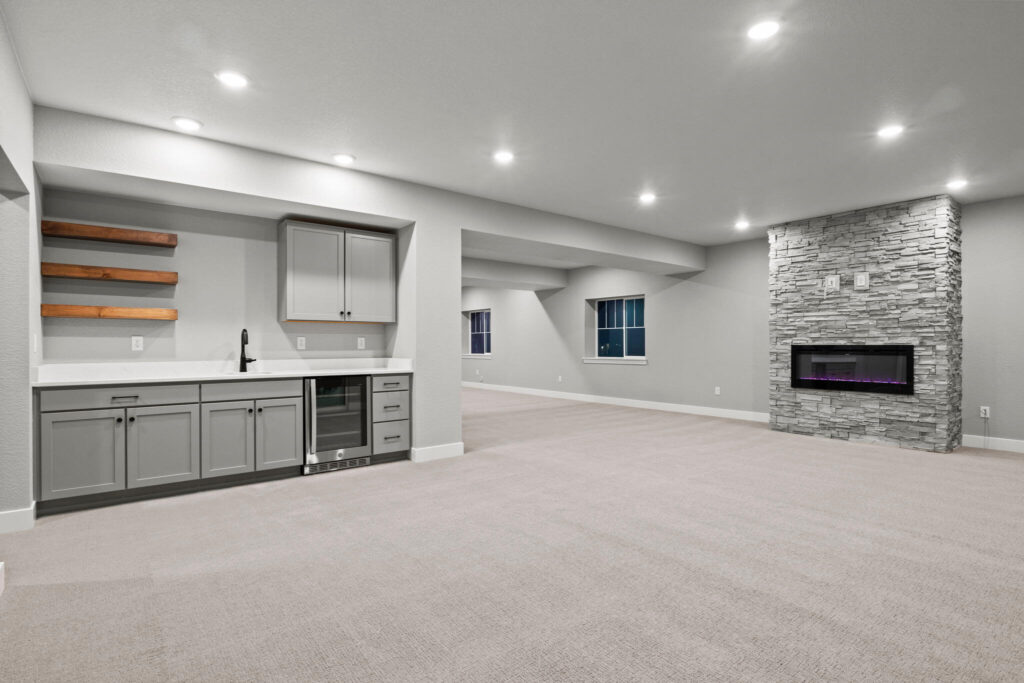 Basement lounge area with a small kitchenette, floating shelves, and stone wall fireplace.