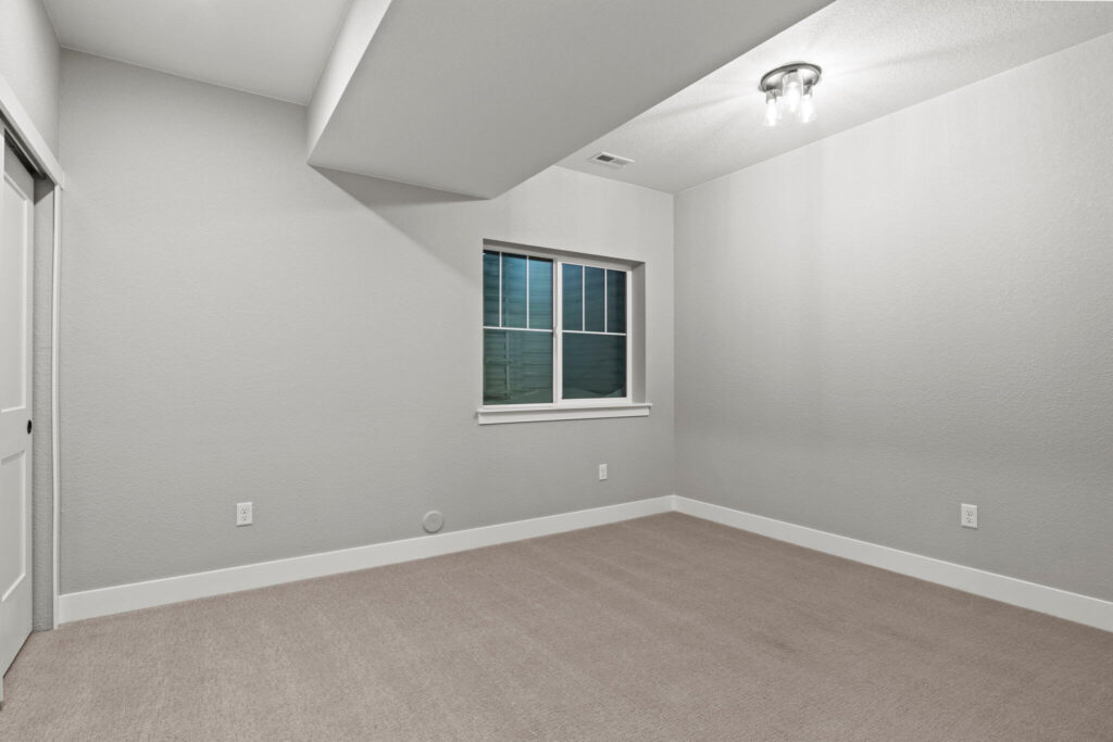 Empty carpeted bedroom or bonus room with a single window and angled ceiling soffit.