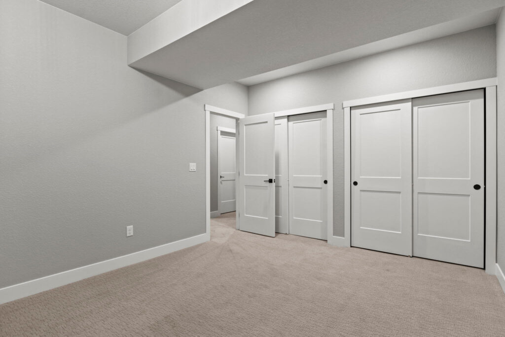 Carpeted room showing an open doorway and paired sliding closet doors under a ceiling beam.