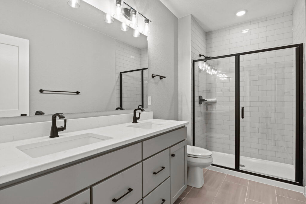 Modern bathroom with double vanity, large mirror, and glass-enclosed tiled shower.