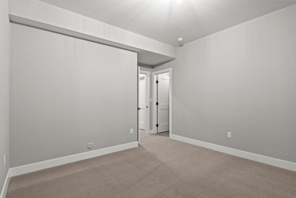 Empty interior room showing doorway, gray walls, carpeted floor, and ceiling bulkhead.