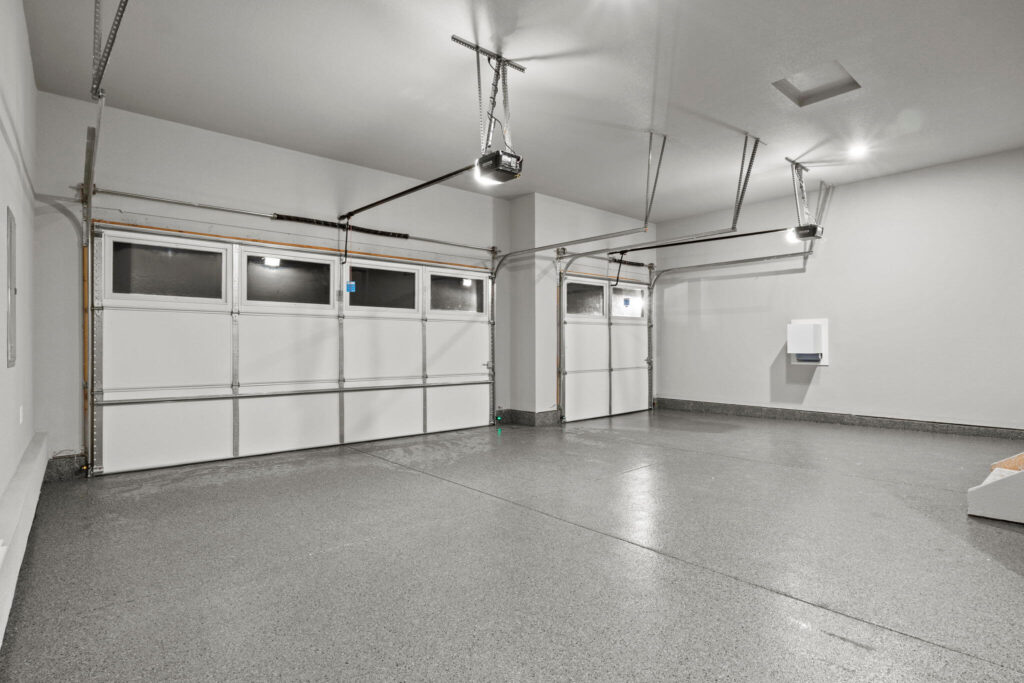 Three-car garage interior with speckled epoxy floor and closed white sectional doors.