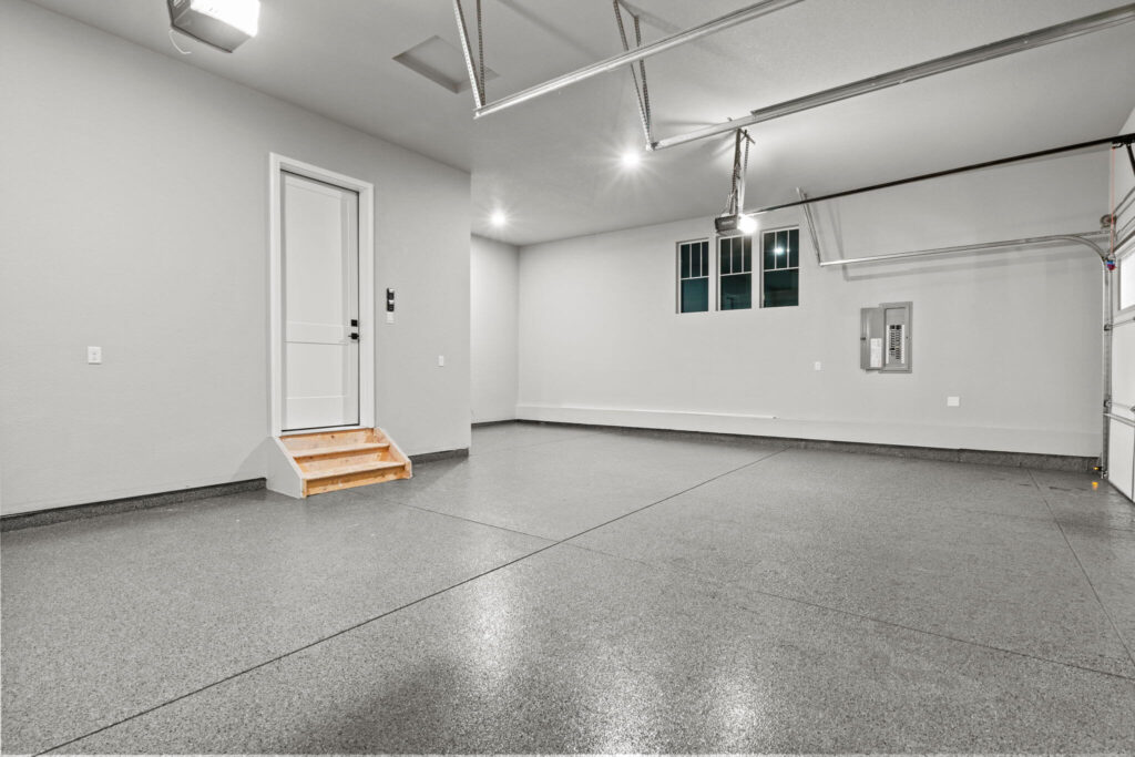 Garage interior viewed from opposite corner showing entry door, small windows, and finished floor.