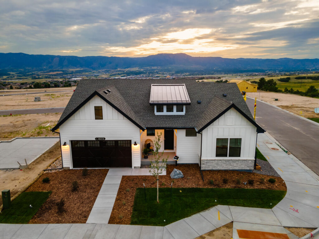 Aerial front view of a single-story white house with dark roof, garage, and surrounding lots.