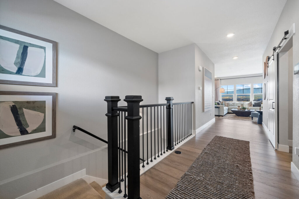 Interior hallway with wood-look flooring, black stair railing, and living area visible at the far end.
