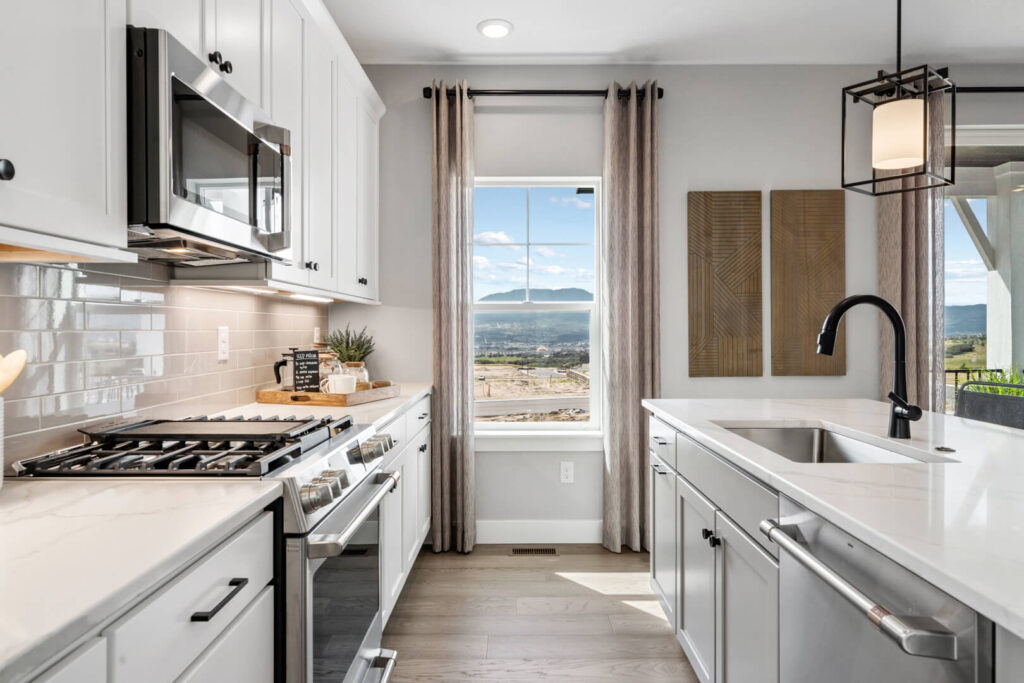 Galley-style kitchen view with stove, microwave, sink island, and window showing an outside view.