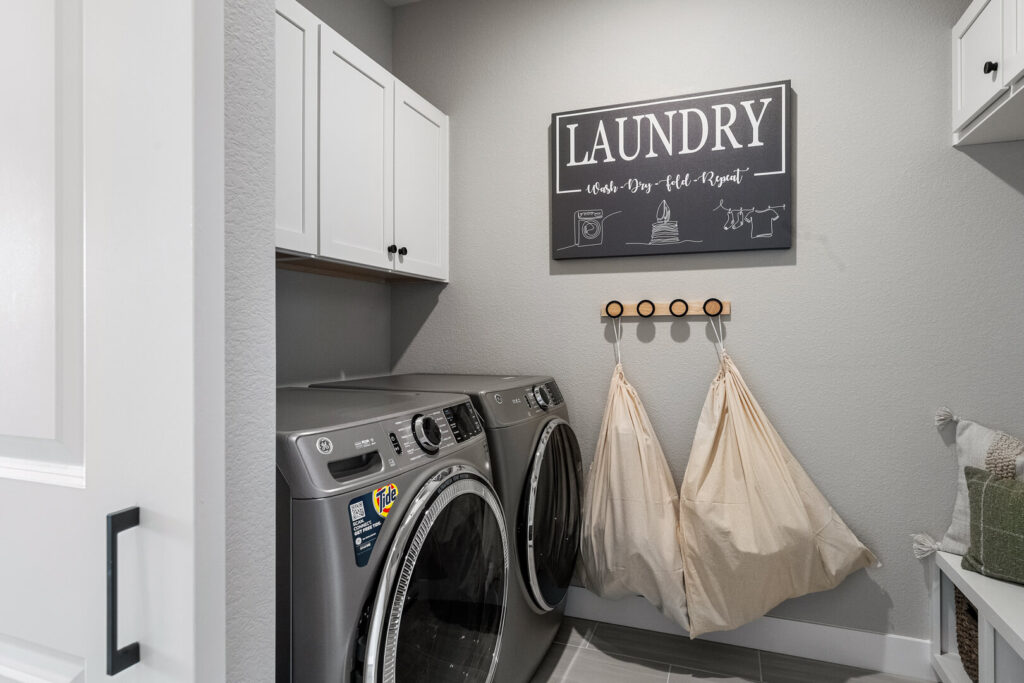 Small laundry room with front-loading washer and dryer, wall cabinets and hanging laundry bags.
