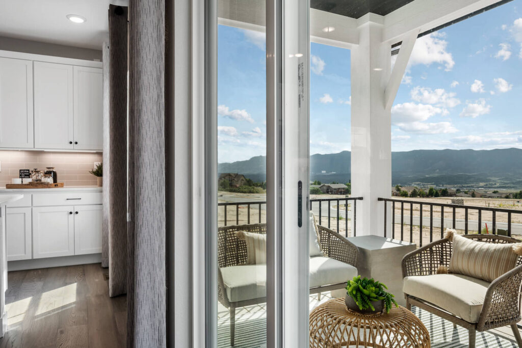 Sliding glass door opening to a covered balcony with wicker chairs and mountain view.