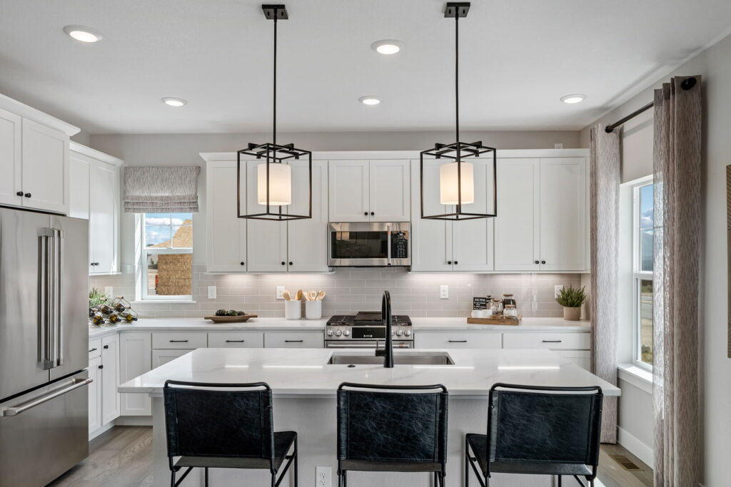 Modern kitchen with large island, three black bar stools, and two geometric pendant lights.