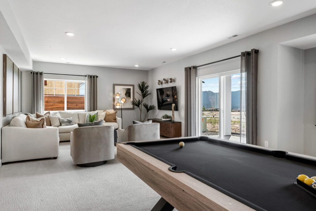 Light-filled living area with sectional sofa, round chairs, and a pool table in foreground.