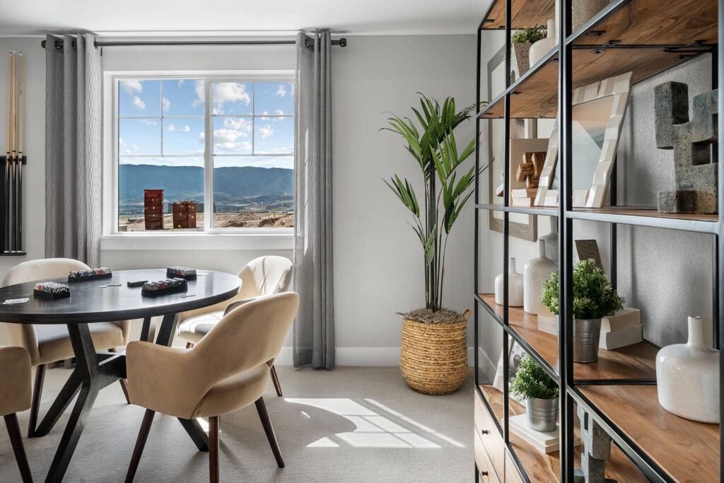 Sunlit game nook with round table, beige chairs, shelving unit, and a window view of hills