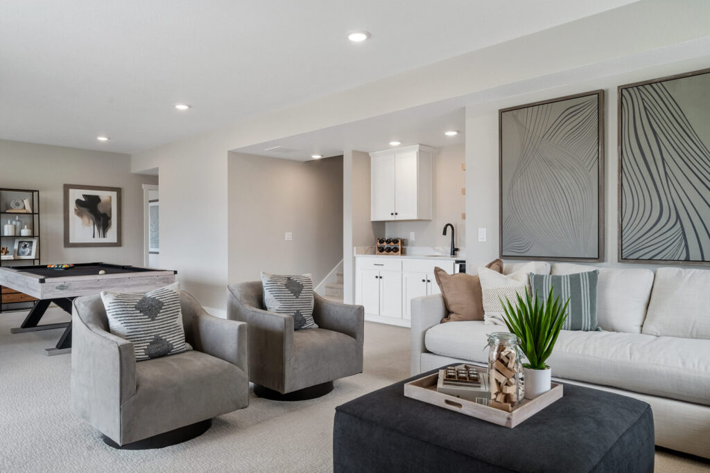 Open basement lounge with two gray armchairs, sofa, and visible pool table area beyond