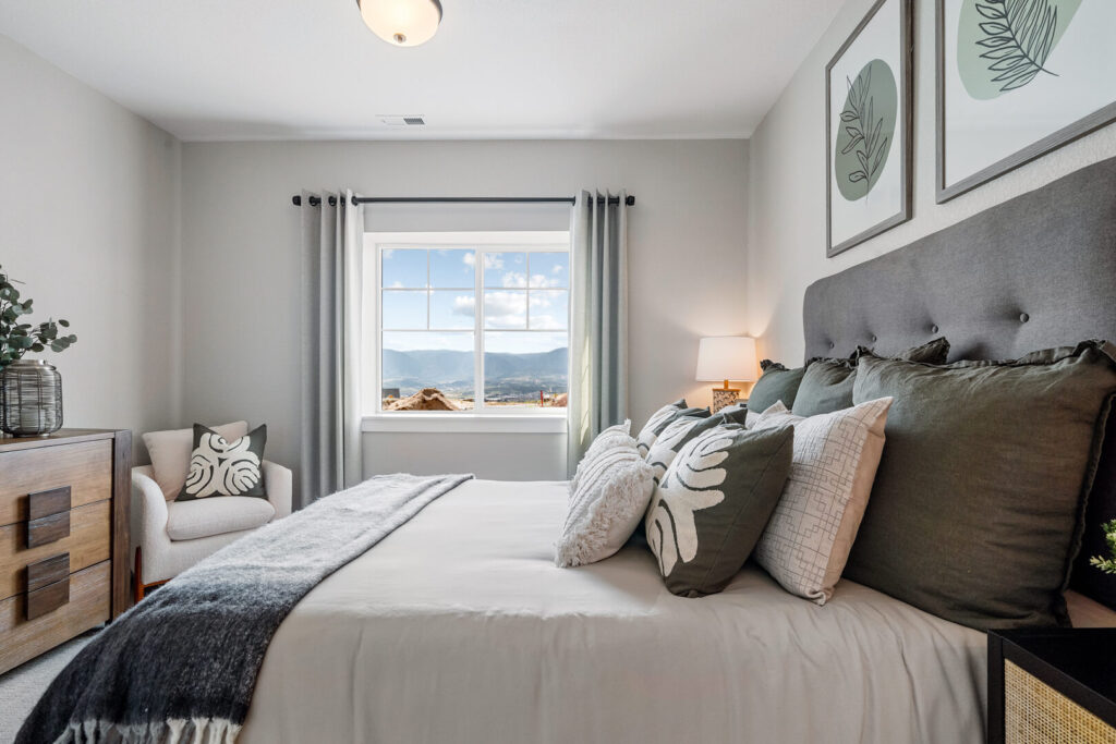 Bedroom with a bed facing a window that shows a distant mountain view and neutral decor.