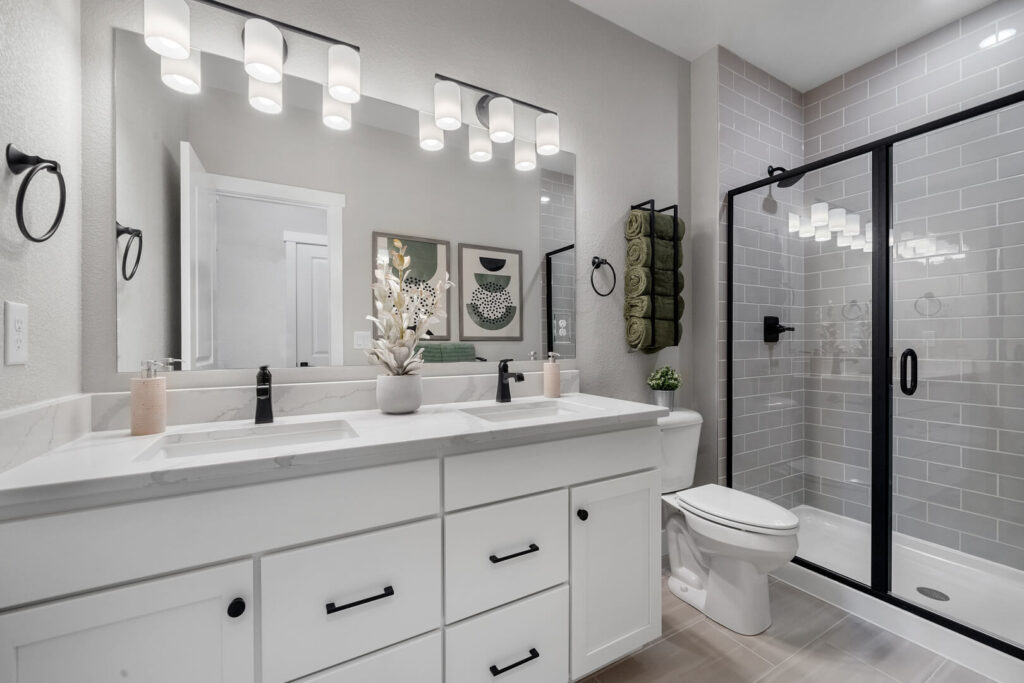 Bright modern bathroom with double sink vanity, large mirror, and glass-enclosed shower.
